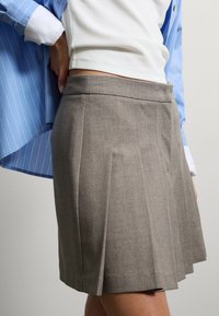 Falda gris con pliegues hecha de tela texturizada, con una cintura ajustada y sutiles detalles de costura. Combinada con una camisa de rayas azul.