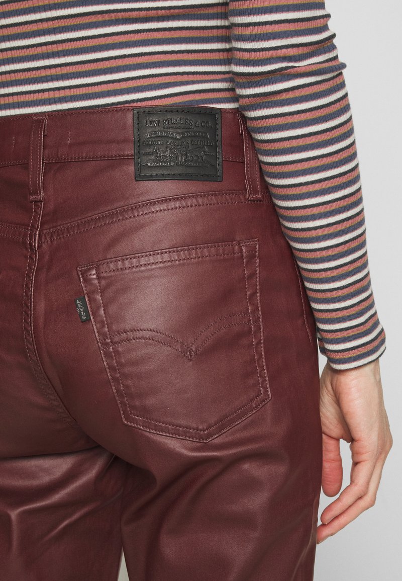 Bordeauxfarbene Denim-Jeans mit einem schwarzen Leder-Logo-Patch, zwei Gesäßtaschen und einer glatten Textur. Der obere Teil hat mehrfarbige horizontale Streifen.