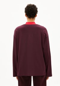 Oversized langebloemig shirt in diep bordeauxrood met een rode geribbelde kraag, met een gladde textuur en een ontspannen pasvorm, gezien van achteren.