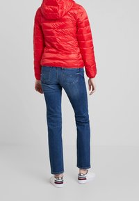 Czerwona pikowana kurtka z kapturem, połączona z niebieskimi spodniami typu straight leg w średnim odcieniu i białymi trampkami z błyszczącymi srebrnymi akcentami.