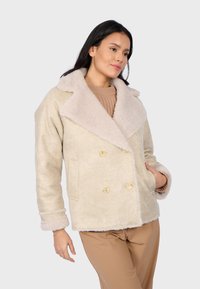 Cappotto beige doppiopetto con colletto peloso, dotato di grandi bottoni e tasche laterali. Tessuto morbido e testurizzato con vestibilità comoda.