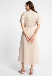 Beżowa sukienka midi z krótkimi rękawami, z teksturowanej tkaniny z delikatnymi kropkami, z elastycznym pasem i prostym krojem. Różowe sandały na obcasie.