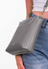 Šedá vegan kožená crossbody taška se strukturovaným tvarem, s hladkým povrchem, jemným logem a stříbrnými detaily.
