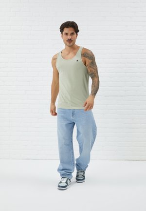 Débardeur en coton vert clair avec un col rond, ornée d'un petit logo noir sur la poitrine, associé à un jean bleu ample et des baskets.
