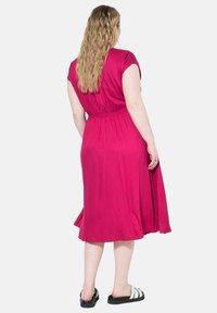 Abito midi fucsia con maniche corte, vita arricciata, tessuto fluido e gonna svasata, abbinato a sandali scivolati bianco e nero.