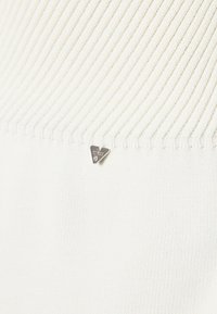 Weißer Strickpullover mit geripptem Muster. Silbernfarbener, dreieckiger Metalllogo-Akzent nahe dem Saum. Glattes Material mit einem weichen Erscheinungsbild.