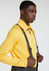 Top amarillo de manga larga con cuello alto, que presenta un cierre con cremallera y una cinta negra con el logo "Oneill", combinado con pantalones oscuros.