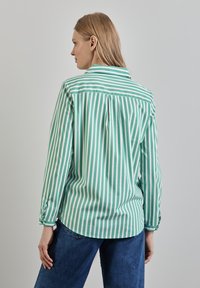 Camisetta a maniche lunghe a righe verdi e bianche con colletto classico, polsini abbottonati e orlo leggermente curvato. Tessuto di cotone liscio.