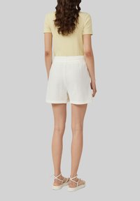 Białe, teksturowane szorty z elastyczną talią, w połączeniu z jasnoniebieską, prążkowaną bluzką oraz beżowymi sandałami na paski, widok z tyłu.