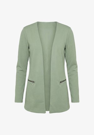 Lichtgroene blouse met lange mouwen, open voorkant, structuur in de stof en twee horizontale ritssluitingen aan de taille.