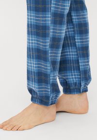 Μπλε καρό πιτζάμα με μαλακό ύφασμα και ελαστικά μπατζάκια. Διαθέτει ένα μείγμα ανοιχτόχρωμων και σκούρων μπλε τετραγώνων με λευκές γραμμές.