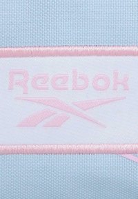 Tela texturizada de color azul claro con una etiqueta blanca y rosa cosida que muestra el nombre y el logo de la marca "Reebok".