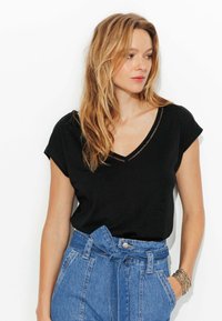 Haut noir à manches courtes en V avec un motif texturé le long de l'encolure, associé à un pantalon en denim bleu clair taille haute.