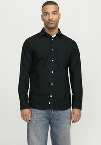 Schwarzes Langarmhemd aus weichem Stoff, mit Knopfleiste, einer Brusttasche und lockerer Passform, kombiniert mit hellen, ausgebleichten Jeans.