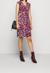 Röd blommig omlottklänning med korta ärmar, strukturerat tyg, knälång, som parats ihop med bruna klackstövletter och en svart axelväska.