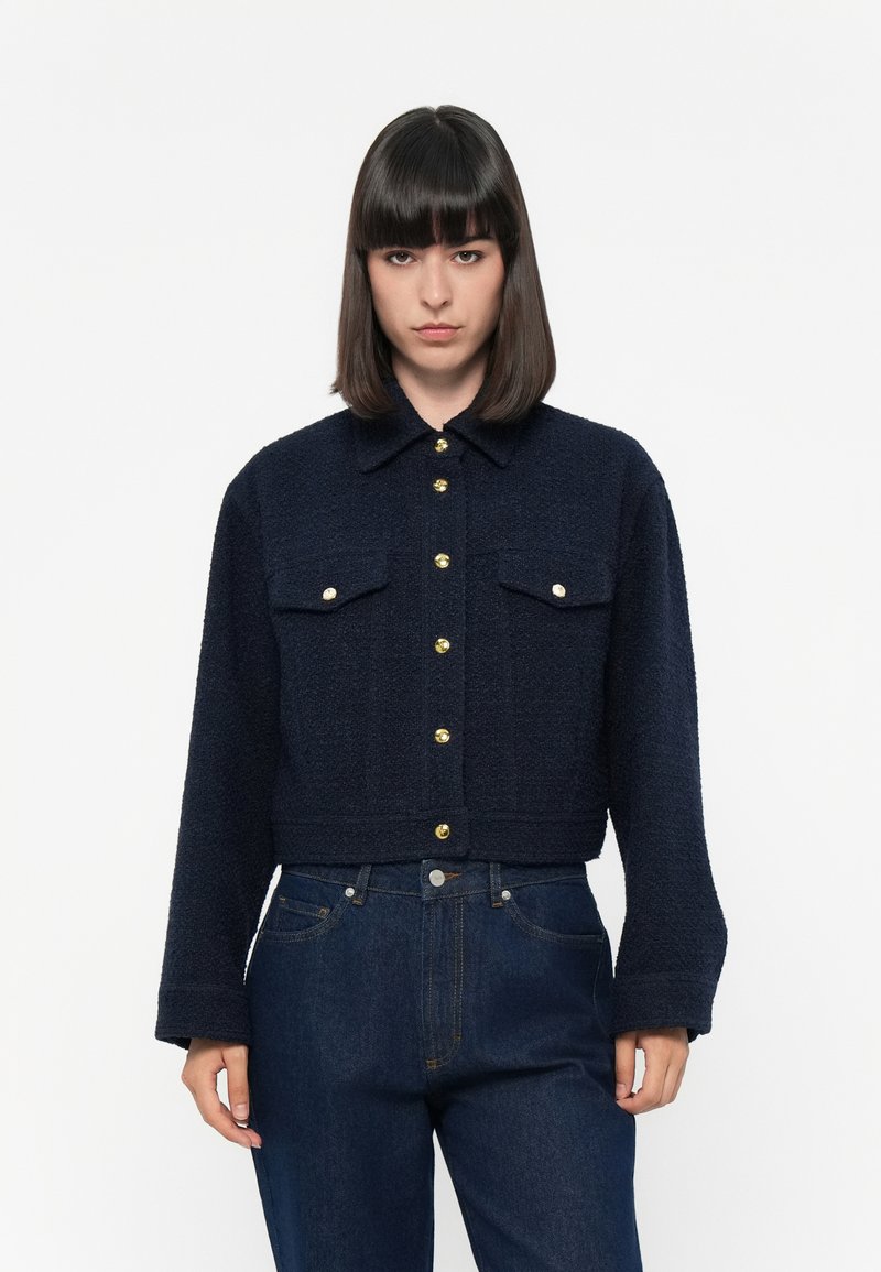 Navy blue cropped jacket in textured fabric, featuring a button-up front, two chest pockets, and gold button accents.