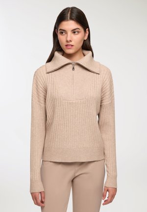 Maglione beige a maglia con colletto alto, chiusura lampo frontale e texture a coste. Presenta maniche lunghe e orlo cropped con taglio dritto.