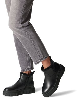 Bottes noires en cuir avec bord en fausse fourrure, fermeture éclair latérale et semelle en caoutchouc épaisse, accompagnées de jeans gris cropped.