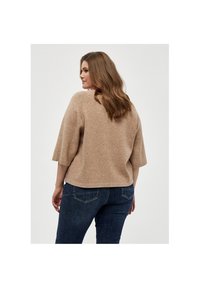 Beiger Wollpullover mit kurzen, glockenförmigen Ärmeln, leicht verkürztem Schnitt und weicher Textur, kombiniert mit dunkelblauen Jeans.