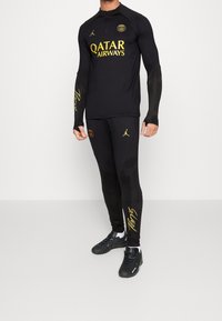 Černý sportovní oblek s dlouhými rukávy a přiléhavými legínami. Obsahuje žlutý nápis "QATAR AIRWAYS" a logo Paris Saint-Germain.