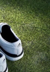 Par av vita Adidas-sneakers med svarta detaljer som vilar på grön gräsmatta.