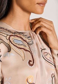 Bluse aus leichtem pinkem Stoff mit filigraner Paisley-Stickerei in Braun, Blau und Gelb. Weicher Griff mit gerafftem Ausschnitt-Detail.