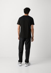 Camiseta de algodón negra de manga corta, combinada con pantalones cargo negros que tienen bolsillos laterales y zapatillas deportivas blancas. Diseño minimalista.