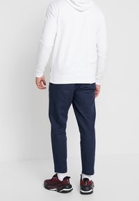 Biała bluza z kapturem o prostym wzorze, w zestawieniu z granatowymi zwężającymi się spodniami i czarno-wiśniowymi butami, prezentowana z tyłu.