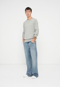 Svetle šedý pletený svetr s ribovanou strukturou, spojený s volnými světle modrými džíny. Bílá teniska doplňuje celý outfit.