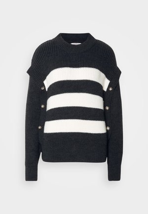 Pull rayé noir et blanc avec une texture côtelée, présentant un col haut et des accents de boutons décoratifs sur le côté.