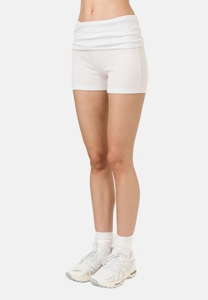 Valged sportlikud lühikesed püksid laia, volditud vöökohaga. Tekstuuriga kangas. Koos valgete jooksujalatsite ja sokkidega. Minimalistlik disain.