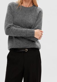 Harmaa villapaita, jossa on pyöreä pääntie ja pitkät hihat, yhdistettynä mustiin housuihin ja mustaan vyöhön, jonka soljessa on kultaista metallia.