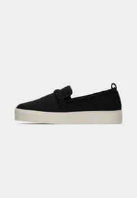 Black slip-on shoes with a textured fabric upper, featuring a braided accent and a white rubber sole. Minimalist design with no laces.