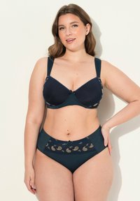 Laivastonsininen liivi pehmeillä kupeilla ja leveillä säädettävillä olkaimilla, jossa on koristeellisia paisley-kuvioita kullassa ja sinisessä. Korkeavyötäröiset yhteensopivat alushousut.