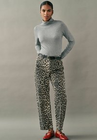Grauer langärmeliger Rollkragenpullover kombiniert mit beigen und schwarzen Leopardenmuster-Hosen, akzentuiert durch einen schwarzen Gürtel und rote Ballerinas.