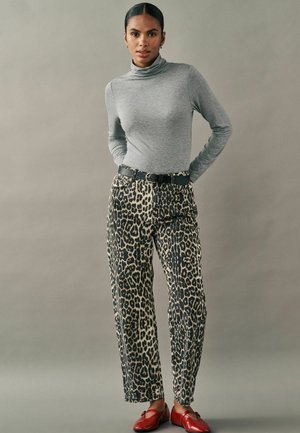 Maglione grigio a maniche lunghe con collo alto abbinato a pantaloni leopardati beige e neri, accentuati da una cintura nera e ballerine rosse.