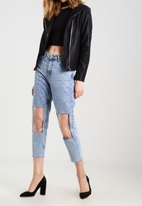 Chaqueta de cuero negra corta, jeans azul claro con paneles transparentes en las rodillas y zapatos de tacón alto negros. Diseño simple con líneas limpias.