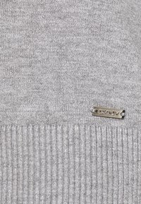 Szary sweter dziany o gładkiej fakturze, z prążkowanym dołem i małą metalową metką z logo DKNY na przodzie.