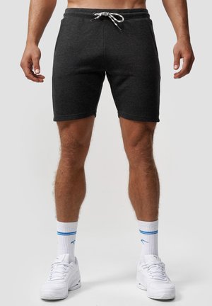 Grå sveder-shorts med snøre i taljen, der har en blød tekstur og en tætsiddende design, parret med hvide sneakers og ankelsokker.