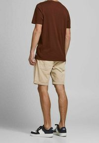 Maglietta a girocollo marrone, pantaloni corti beige con tasche e sneaker blu navy con accenti bianchi, vista da dietro.