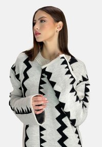 Übergroßer Strickpullover in Creme mit schwarzen Zickzackmustern, mit einem weiten Rundhalsausschnitt und langen Ärmeln mit Ausschnitten. Str Texturierte Oberfläche.