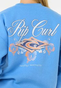 Sudadera azul claro con "Rip Curl" en un guion blanco, un gráfico de diamante con un contorno naranja y patrones florales en naranja y azul.