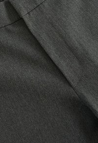 Gros plan d'un tissu gris foncé montrant une couture et un pli sur mesure, mettant en valeur la texture et les détails de la couture.