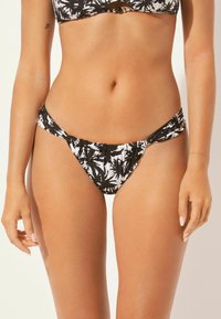 Schwarze und weiße Bikiniunterhose mit einem Palmenblattmuster. Mit einem gerafften Bund und glattem Stoff in einem tiefen Schnitt.