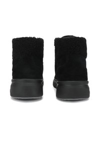 Bottes chelsea en suede noir avec un col en fourrure texturée douce noire et une semelle épaisse et robuste noire. Design simple et moderne.
