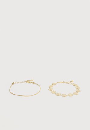 Deux bracelets en or sur un fond blanc ; l'un est une fine chaîne et l'autre présente des motifs floraux liés, tous deux avec des fermoirs réglables.