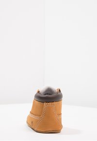 Beżowy skórzany botek za kostkę z brązowym wyściełanym kołnierzem, białym szwem i jasnobeżową podeszwą. Miękka wyściółka wewnętrzna i okrągły kształt noska.