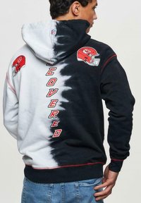 Huppari, jossa on mustavalkea dip-dye -kuvio, NFL-logo, Kansas City Chiefsin kypäräkuva ja sana "COVERED" punaisella.