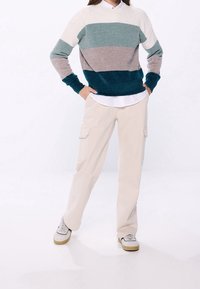 Maglione a maglia con strisce orizzontali in teal, grigio e crema; abbinato a pantaloni cargo beige; include una camicia bianca sotto e scarpe da ginnastica grigie.