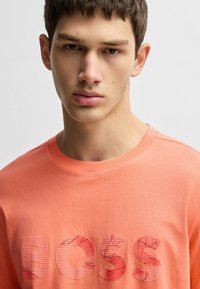 Koralfarvet bomulds t-shirt med et stort, tekstureret "BOSS" logo i gittermønster, rund halsudskæring og korte ærmer. Glat stoffinish.